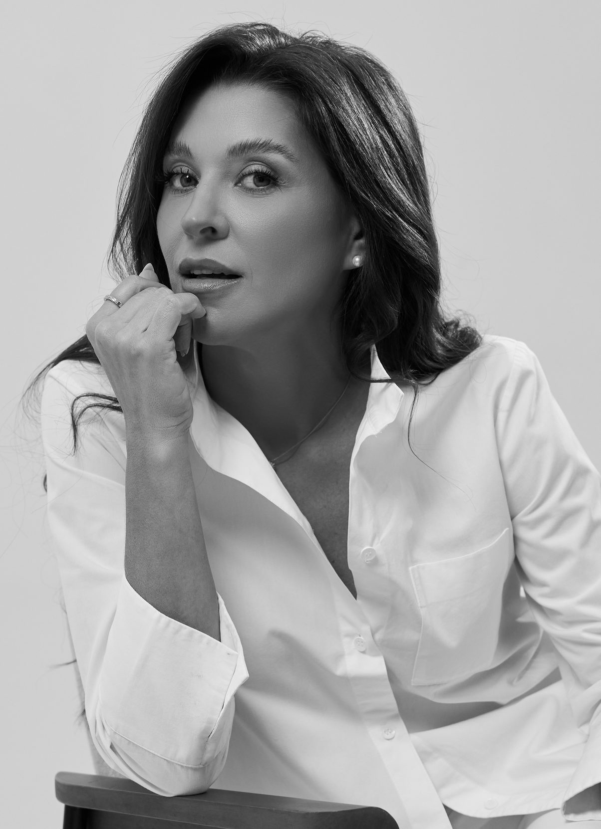 Retrato em preto e branco da Dra. Carolina Rosa de camisa branca, com a mão no queixo