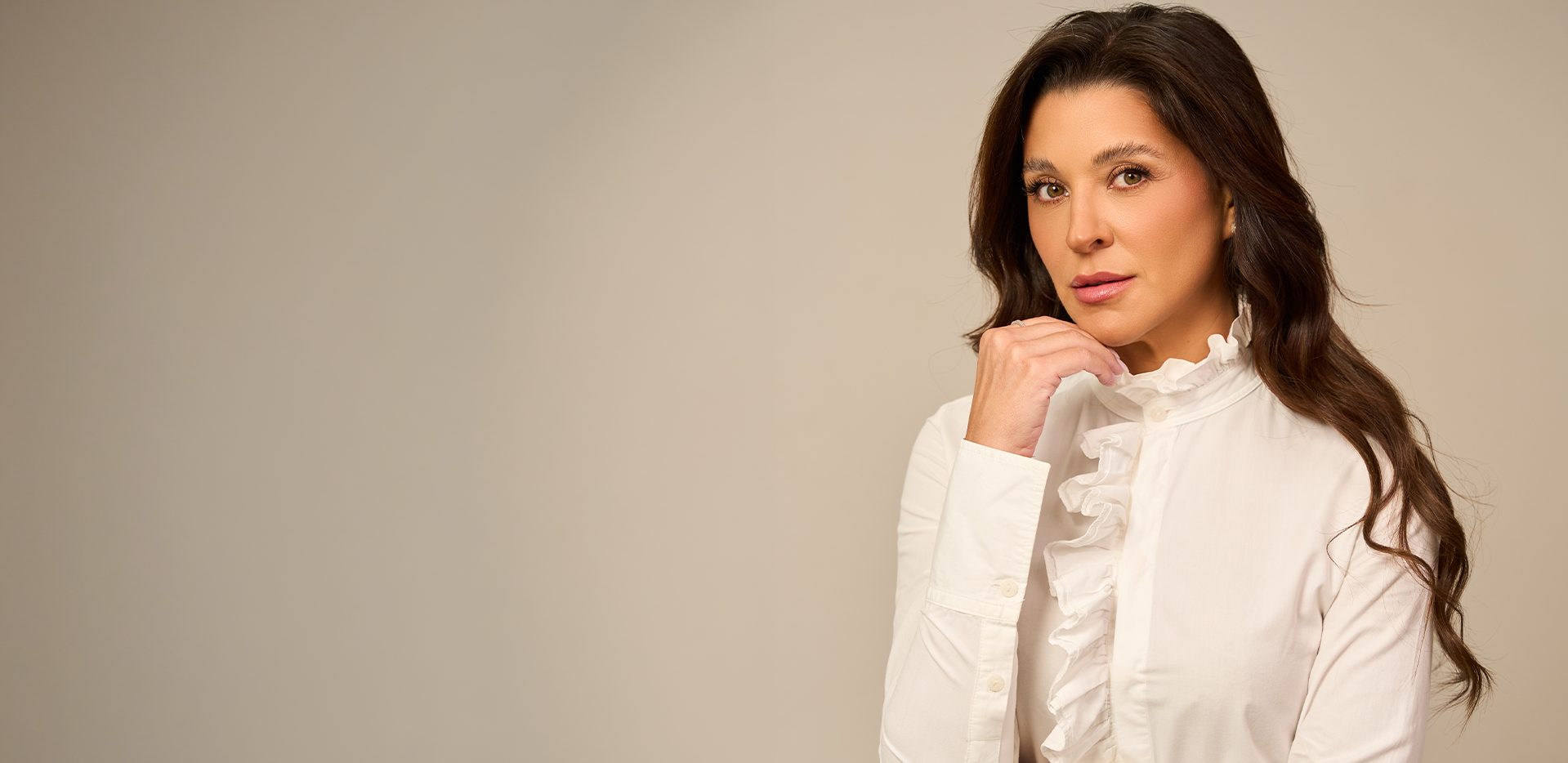 Dra. Carolina Rosa de camisa branca, com a mão no queixo, sobre fundo bege